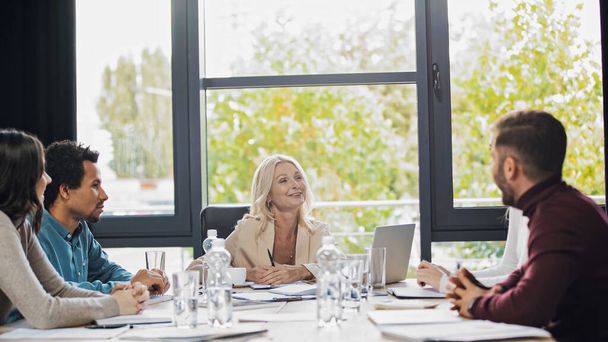 позитивна бізнес-леді середнього віку розмовляє з молодими багатоетнічними менеджерами під час зустрічі
 - Фото, зображення