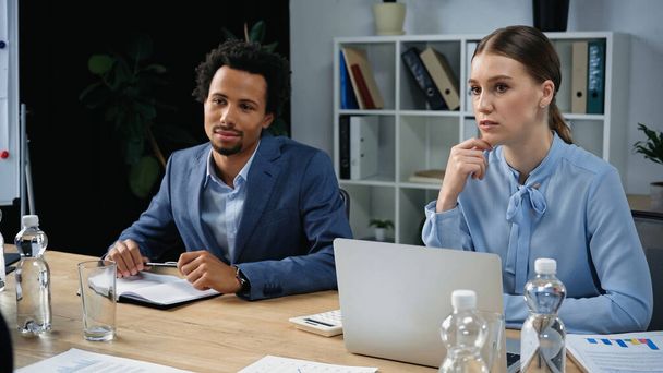 thoughtful interracial business people sitting near laptop and documents in meeting room - Photo, Image