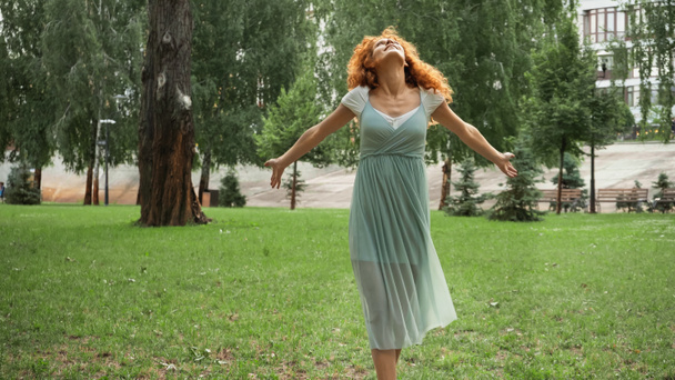 joyful redhead woman in chiffon dress standing in green park  - Photo, Image