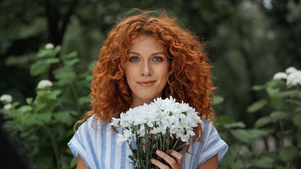 pleased redhead woman holding bouquet of white flowers  - Фото, изображение