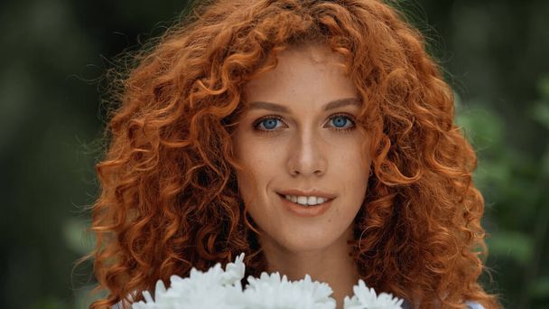 smiling redhead woman with blue eyes near white flowers  - Foto, immagini