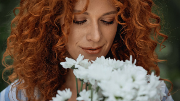close up of curly redhead woman looking at white flowers  - Фото, изображение