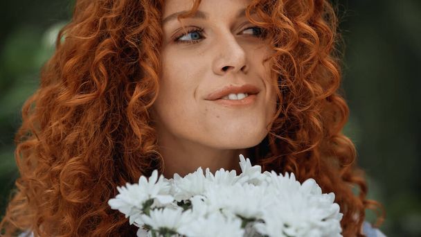 白い花の近くの幸せな赤毛の女性のクローズアップ  - 写真・画像