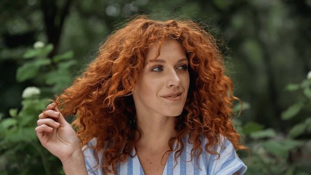 cheerful redhead woman pulling red curly hair - 写真・画像