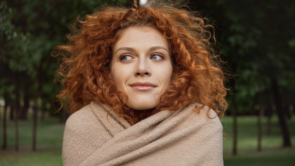 pleased redhead woman with blue eyes covered in blanket outside  - 写真・画像