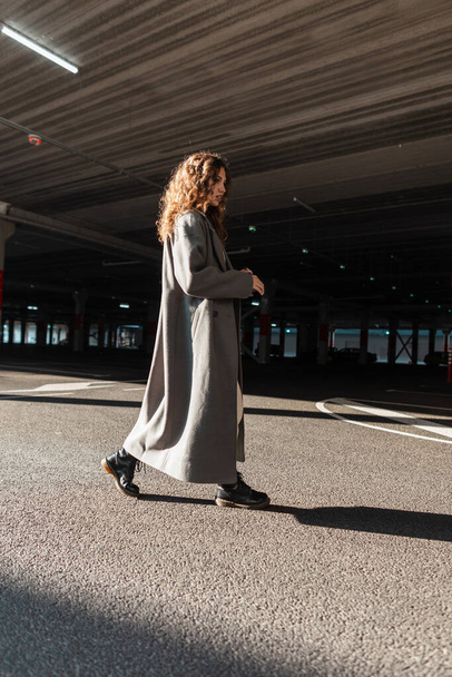 Красивая молодая стильная женщина с вьющимися волосами в моде длинное пальто прогулки по улице на парковке. Городской стиль - Фото, изображение