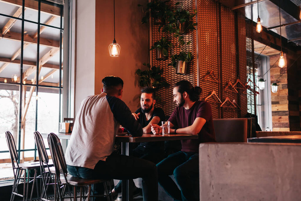 Gruppe junger Männer gemischter Rasse, die sich in einer Lounge-Bar unterhalten. multirassische Freunde beim Kaffeetrinken im Café. Jungs hängen ab - Foto, Bild
