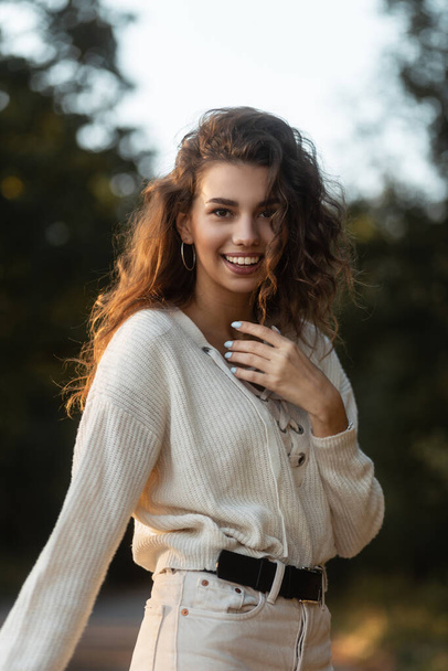 Счастливая женщина с кудрявыми волосами и милой улыбкой с зубами в модном вязаном свитере на улице. Красивое улыбающееся лицо - Фото, изображение