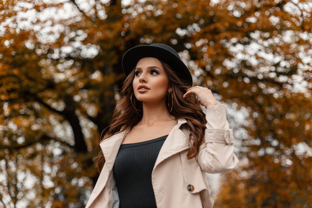 Herbst-Porträt der schönen glamourösen jungen Frau mit lockigem Haar mit Vintage-Hut im grauen modischen Mantel, der draußen mit buntem Herbstlaub spaziert - Foto, Bild