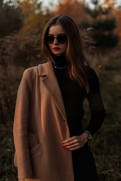 Mode belle femme de style avec des lunettes de soleil vintage dans un manteau beige élégant automne dans l'herbe dans la nature - Photo, image