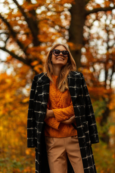 Vidám szép mosolygós lány divat napszemüveg divatos kabát és sárga vintage pulóver sétál a parkban. Boldog női arc - Fotó, kép