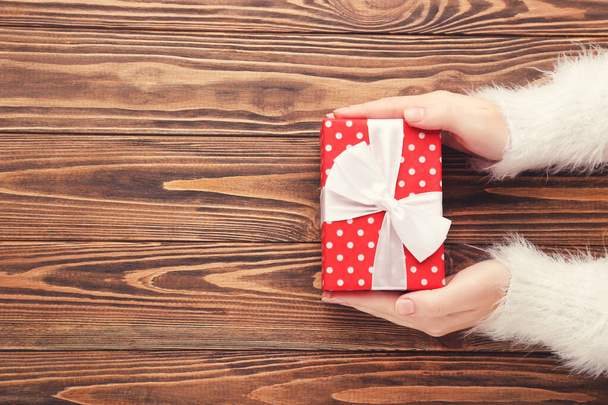 Female hands holding gift box on brown wooden background - Foto, afbeelding
