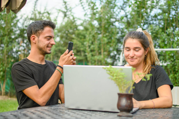 Emotie. Een jonge blanke man die een foto neemt van zijn vriendin die naar haar laptop kijkt. Horizontaal. met kopieerruimte. - Foto, afbeelding