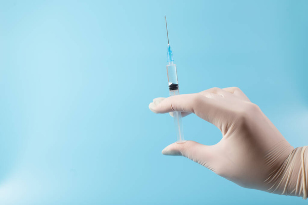 Doctor hands in white gloves holding syringe with vaccine, close up on blue background with copy sapce. - Photo, Image