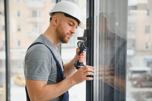 Construction worker using drill while installing window indoors - Fotografie, Obrázek