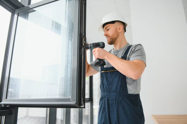 Construction worker using drill while installing window indoors - Valokuva, kuva