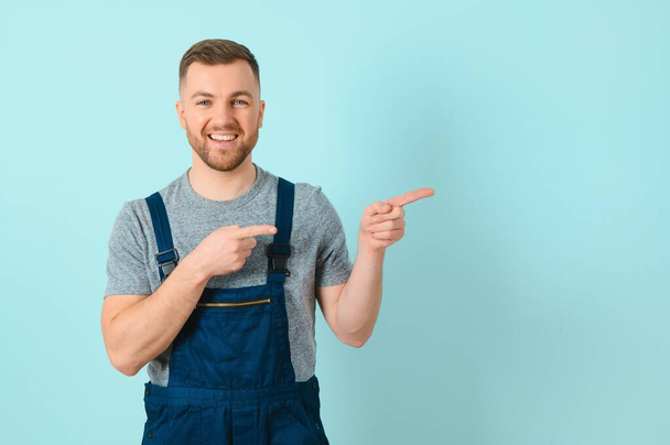 Young electrician man or Craftsmen over isolated blue wall pointing to the side to present a product - Fotografie, Obrázek