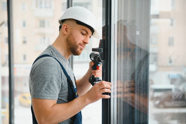 Construction worker using drill while installing window indoors - Foto, imagen