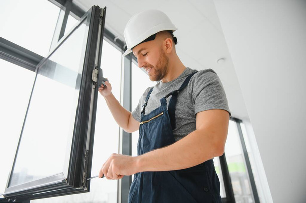Workman in overalls installing or adjusting plastic windows in the living room at home - Foto, Imagen