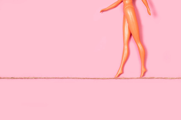 Poupée nue marchant sur une corde sur un fond rose avec espace de copie - Photo, image