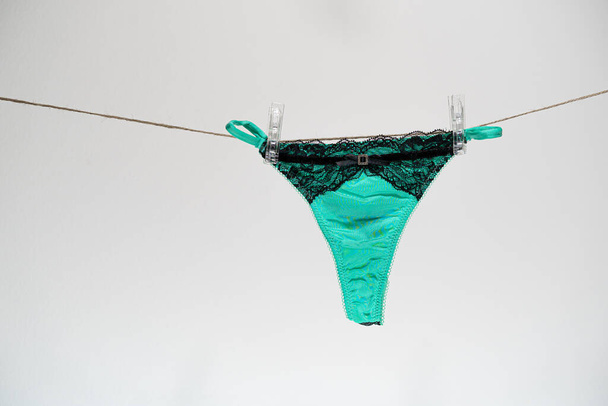 Zelené dámské tanga kalhotky na prádelní šňůře zapnuté bílými kolíky. Láska, sex a intimní zdravotní koncept. - Fotografie, Obrázek