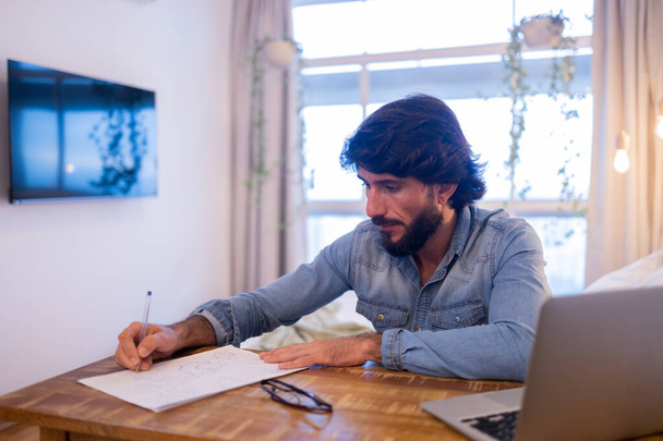Mladý obchodník pracující doma ve své ložnici s laptopem a papíry na stole. Šedý zápisník pro práci. Koncept domácí kanceláře. Kvalitní fotografie - Fotografie, Obrázek