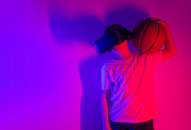 Fiatal fiú kosárlabdával, aki VR szemüveget játszik neon világításon. Emberek, technológia, sport és kibertér koncepció - Fotó, kép
