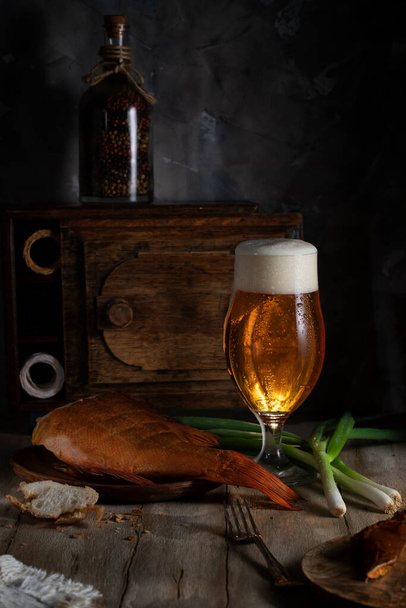 Glass goblet with beer, green fresh onion and smoked fish on rustic table - Photo, Image