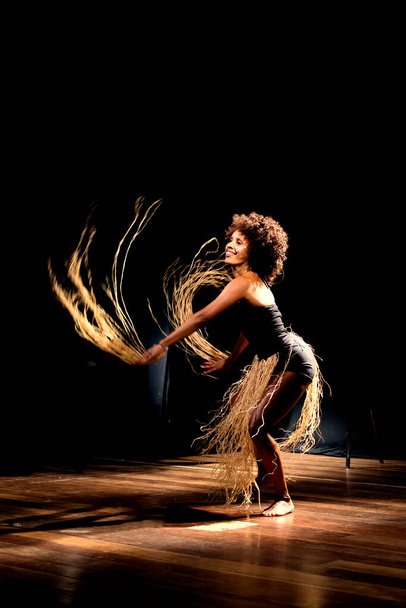 黒の背景と藁のアクセサリーを持つ劇場でコンテンポラリーダンサーのダンス。サルバドール・バイア・ブラジル. - 写真・画像