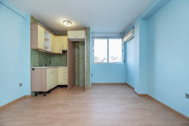 Small studio with a kitchen in one corner and a green tiled wall and the rest of the walls painted sky blue - Photo, Image