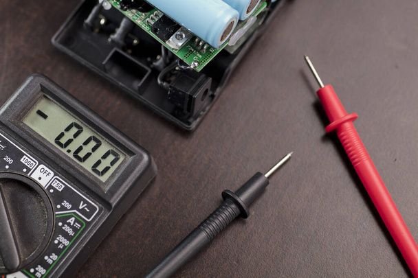volt meter, red positive pole, black negative pole, on work table with batteries 18650 model - Foto, Imagen