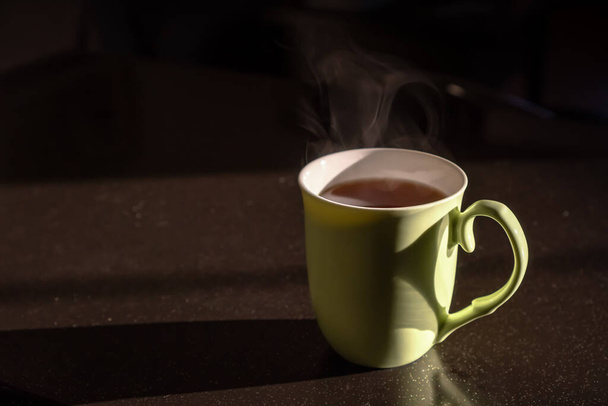 Groene beker met warme thee in het zonlicht. Lifestyle binnenlandse foto concept - Foto, afbeelding