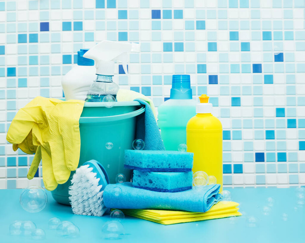 Reinigingsmiddelen en wasmiddelen in een emmer, reinigingsaccessoires, blauwe achtergrond met zeepbellen - Foto, afbeelding