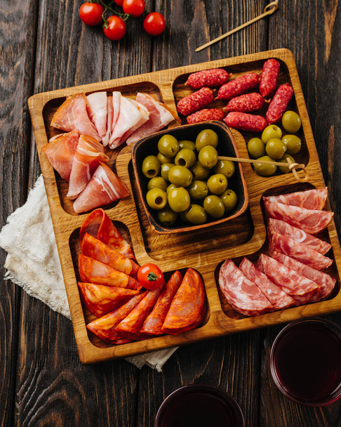 Snacks pour vin sur une planche en bois. Menazhnitsa aux saucisses, olives et tomates cerises. - Photo, image