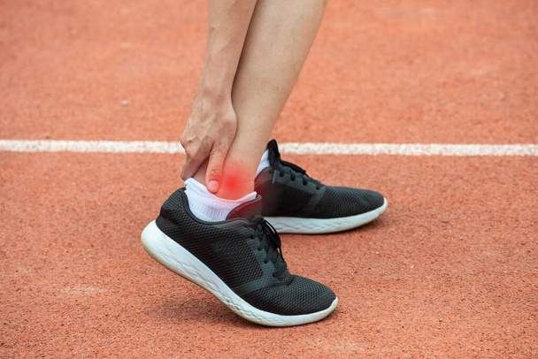 Close up of runner woman holding her ankle, suffering from ankle pain after running. Conceptual of injury from running workout. - Фото, изображение