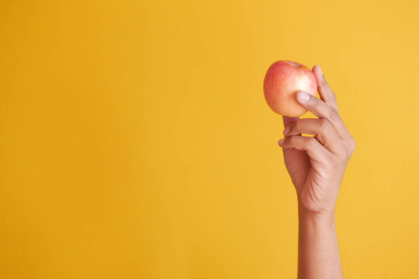 child boy hand hold a apple on yellow background  - Foto, imagen