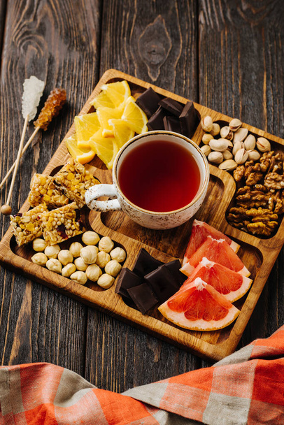 Menazhnitsa auf einem hölzernen Hintergrund. Köstlicher Tee, Nüsse und Schokolade auf einem quadratischen Holzteller. Hochwertiges Foto - Foto, Bild