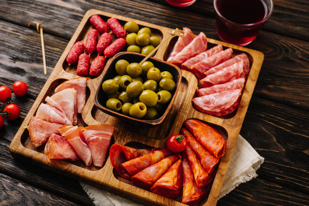 Los tentempiés para el vino en la tabla de madera. Menazhnitsa con salchichas, aceitunas y tomates cherry. Foto de alta calidad - Foto, Imagen