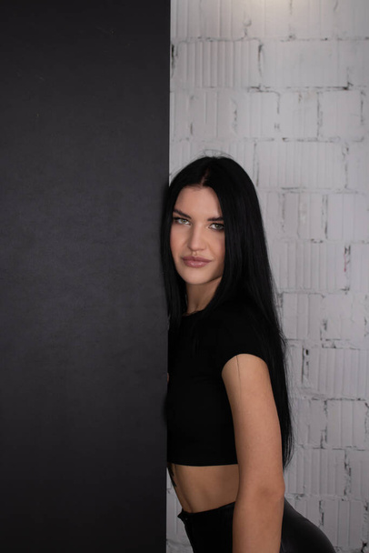 mujer morena sexy en negro contra fondo de pared de ladrillo blanco. retrato de moda femenina - Foto, Imagen