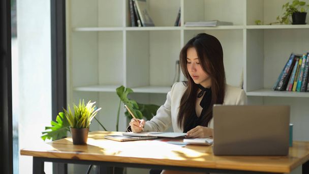 Die schöne asiatische Geschäftsfrau arbeitet an ihrem Schreibtisch im Büro. Chefin oder Managerin notiert sich Notizen in ihrem Notizbuch. - Foto, Bild