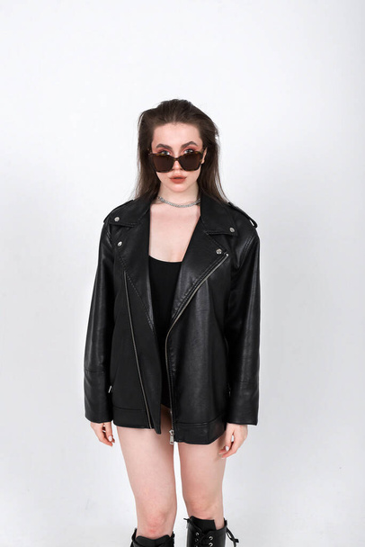 女の子モデルポーズでサングラス黒ボディスーツと黒革のジャケット上の白い背景コピースペースのためのテキスト - 写真・画像