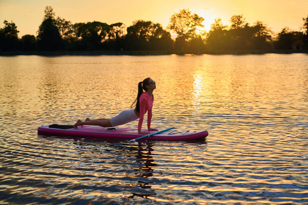 Young athletic woman practising sup yoga during sunset - Photo, image