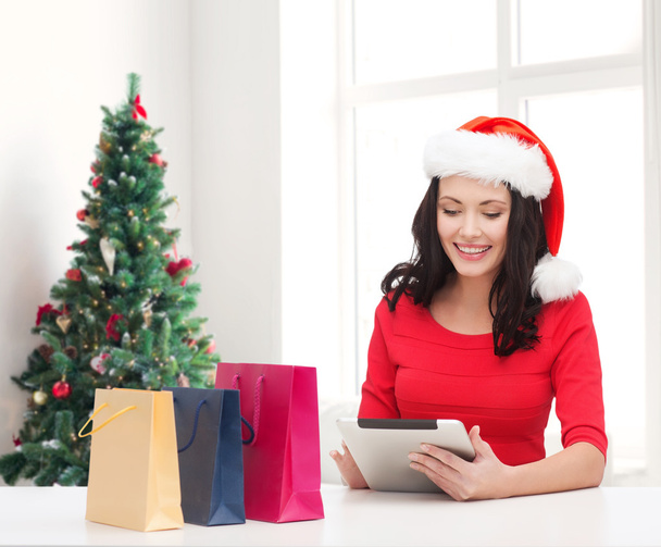 smiling woman in santa hat with bags and tablet pc - Valokuva, kuva