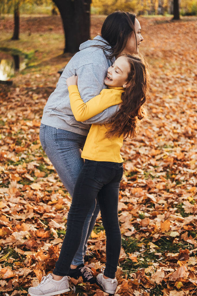 Mère et petite fille s'amusent, s'embrassent dans un parc d'automne. Grande conception pour tous les usages. Souriant enfant heureux. Bonne famille ensemble. - Photo, image