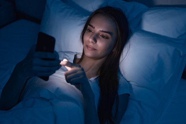 Sleepy woman browsing smartphone in bed - Foto, imagen