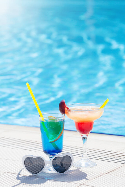 Two colorful cocktail glasses at the edge of swimming pool. With copy space - Photo, Image