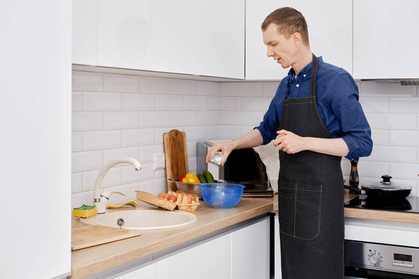 Middle-aged man pours salt making an omelet in the kitchen - Fotografie, Obrázek
