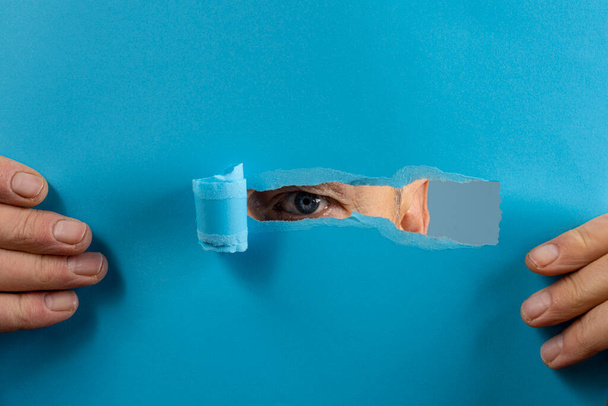 el ojo de un hombre mirando a través de la lágrima en una hoja de papel - Foto, Imagen