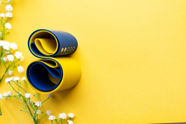 Auf gelbem Grund liegt elastisches Fitness-Band. Acht aus einem Gummiexpander für den Sport. Weißblumen - Foto, Bild