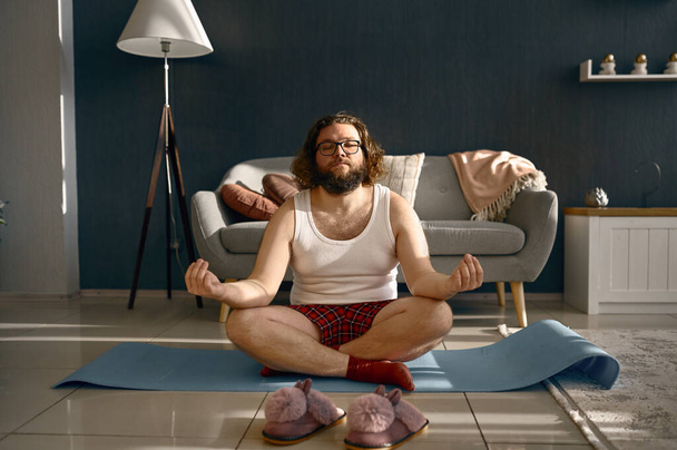 Komik şişman adam evde yoga yaparken meditasyon yapıyor. - Fotoğraf, Görsel